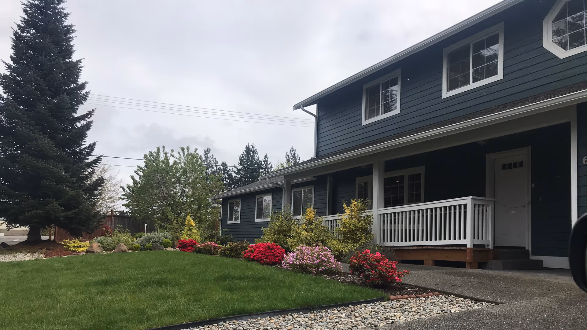 Blue Haven senior living building exterior with a porch, flowering shrubs, and a green lawn.