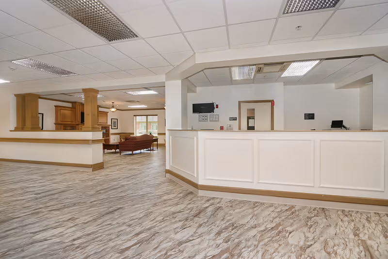 Spacious lobby with white reception desk, seating area, and wood accents inside a senior facility.