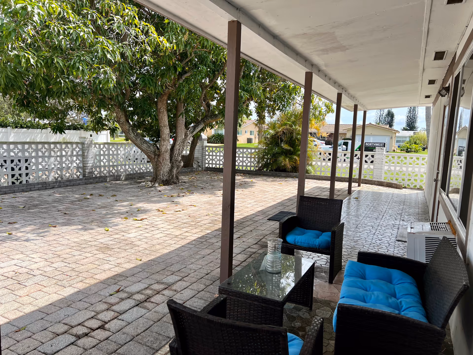 Covered outdoor patio with wicker chairs, blue cushions, glass table, and lattice fence.
