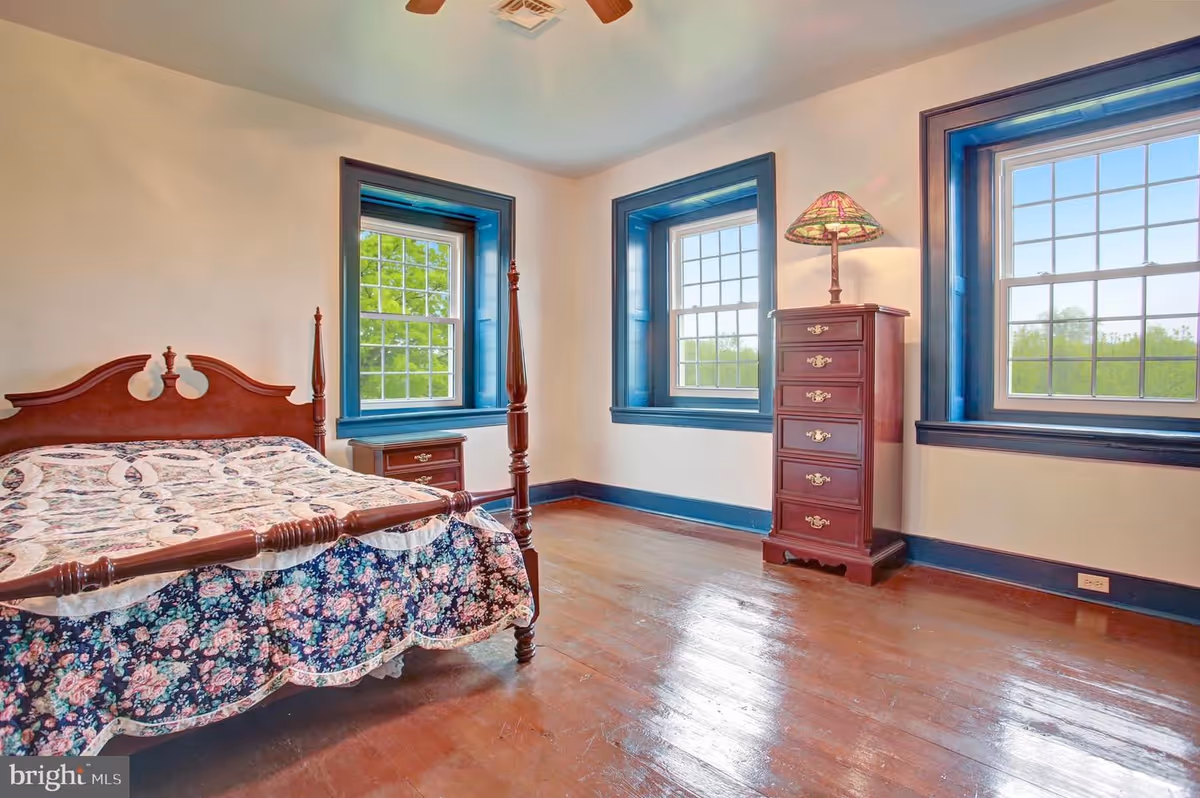 A simple bedroom with a dark wood four-poster bed, dresser, and blue-trimmed windows.