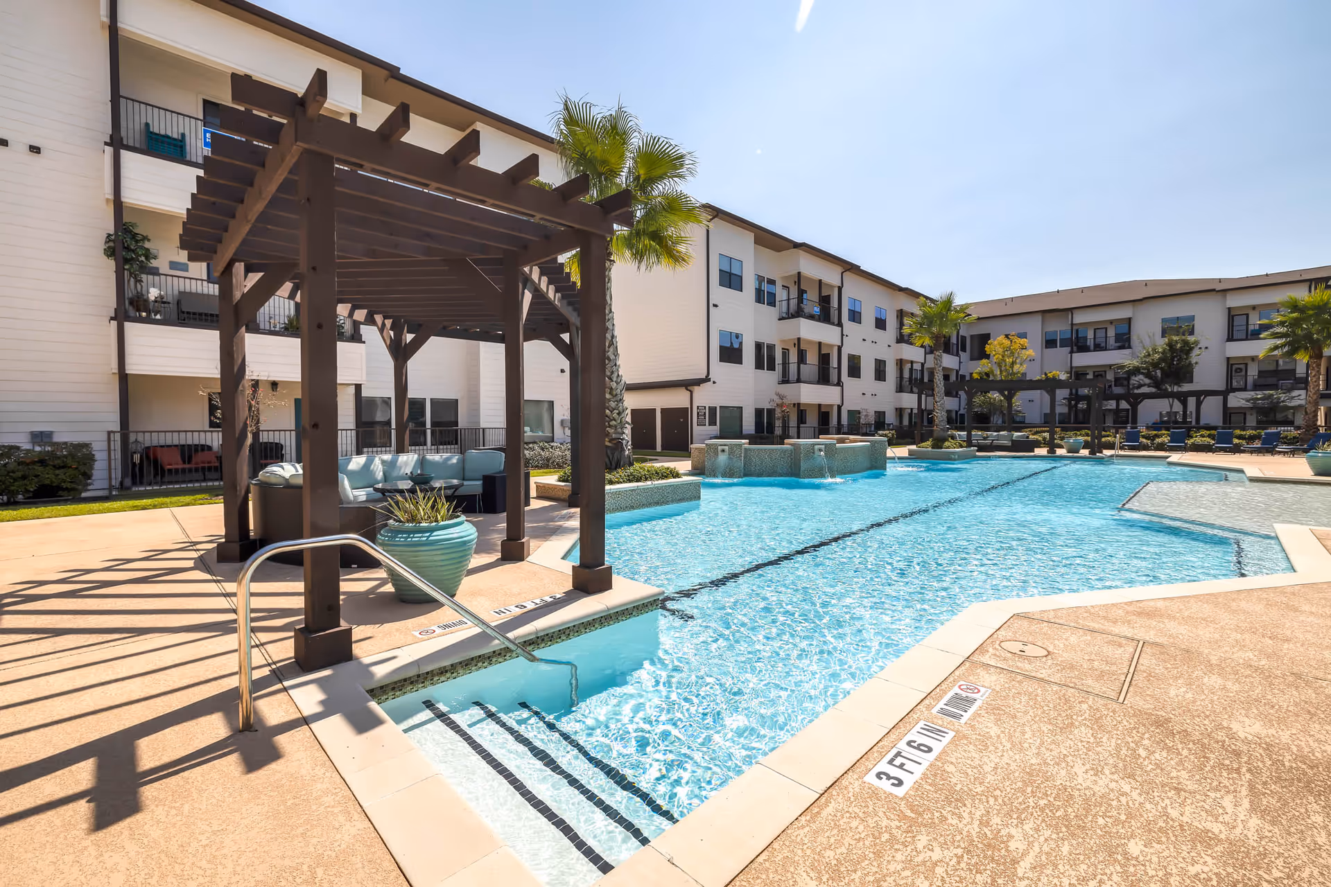 Outdoor swimming pool with a pergola seating area and surrounding three-story apartment building courtyard.