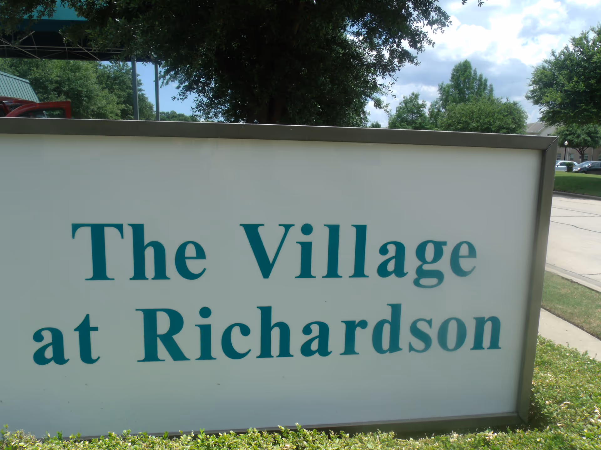 Outdoor sign reads The Village at Richardson with trees and a sidewalk in the background.