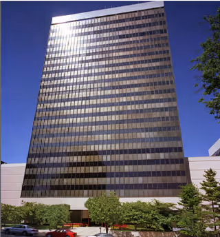 Tall glass office building with trees and a few cars in the foreground.