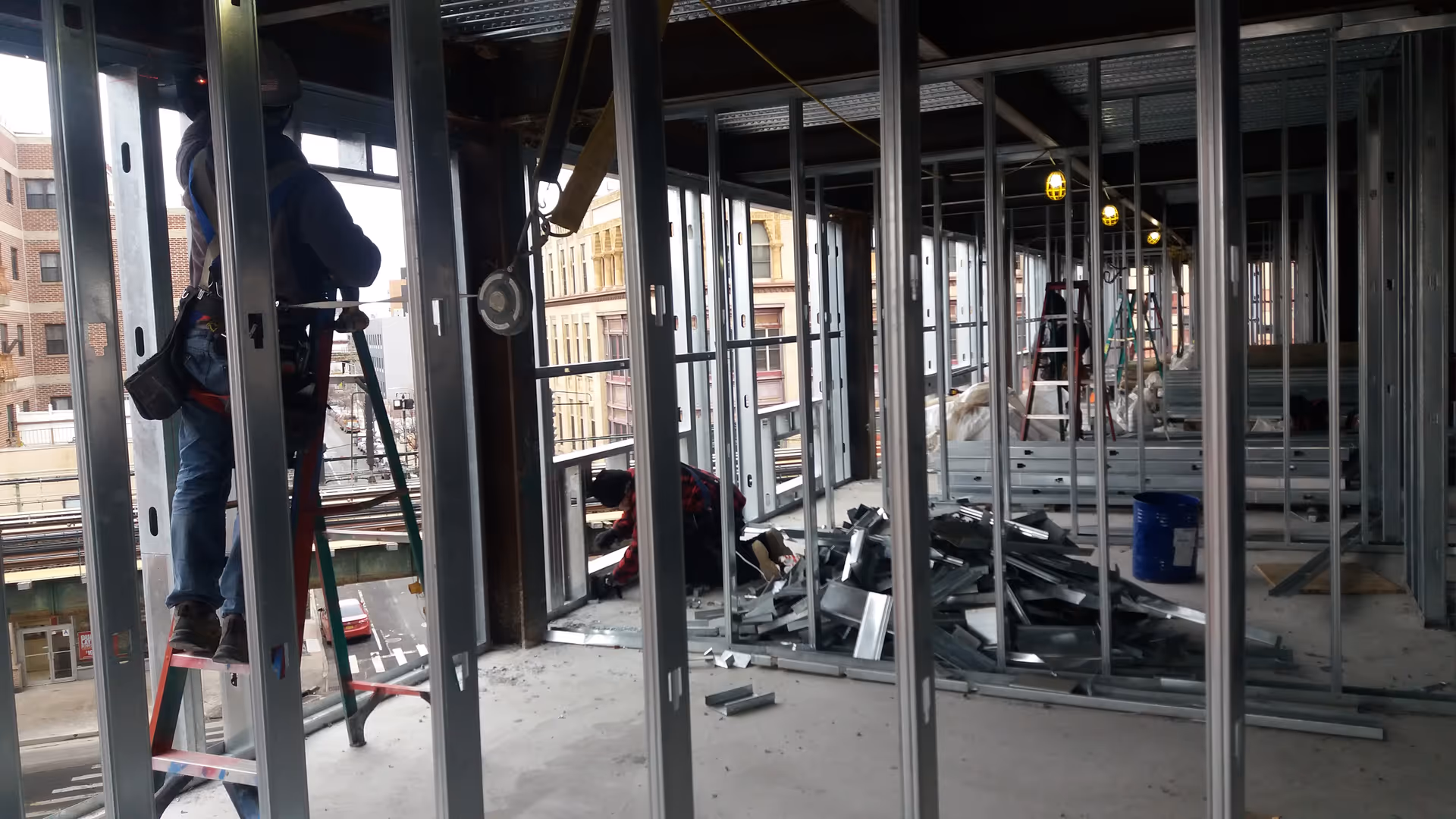 Unfinished interior of a building with metal studs, ladders, and workers.