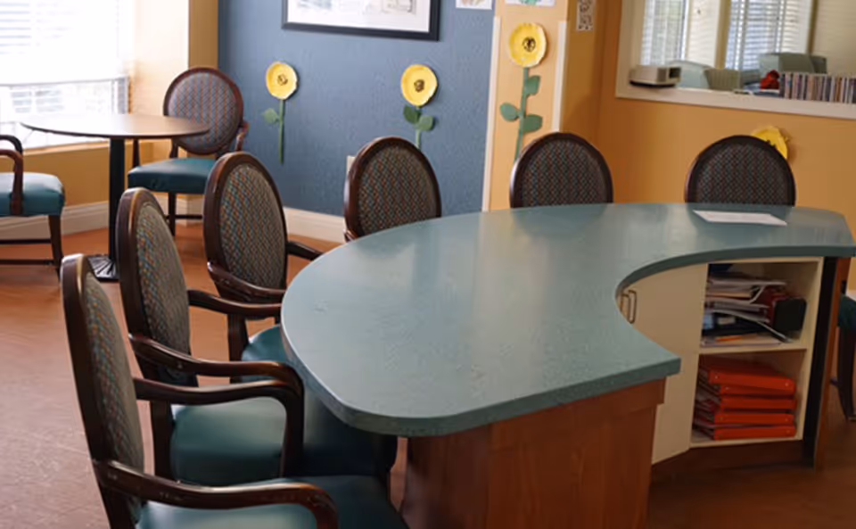 Curved teal reception desk with chairs in a bright senior living common room.