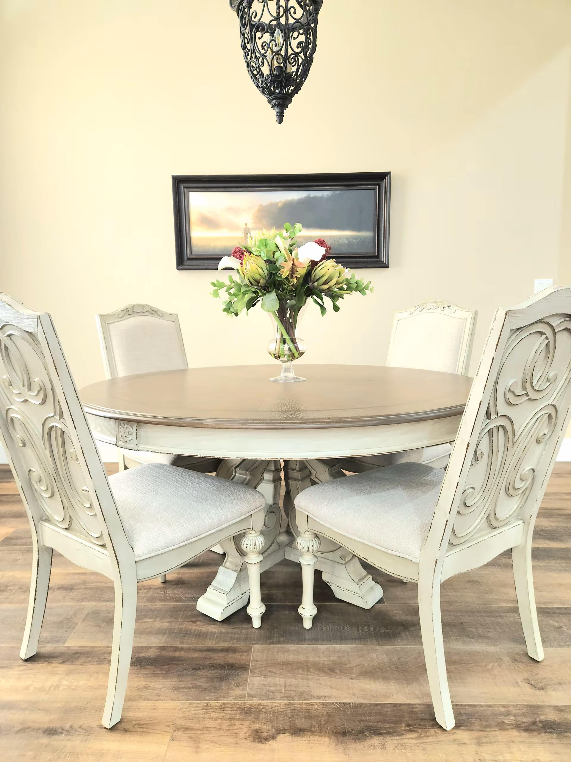 Round dining table with floral centerpiece and ornate cream chairs in a bright dining room.