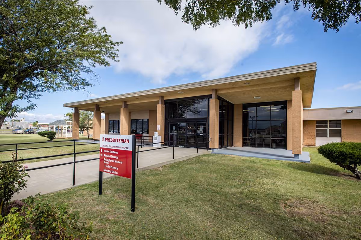Front entrance of a modern medical building with glass doors and a red Presbyterian sign.