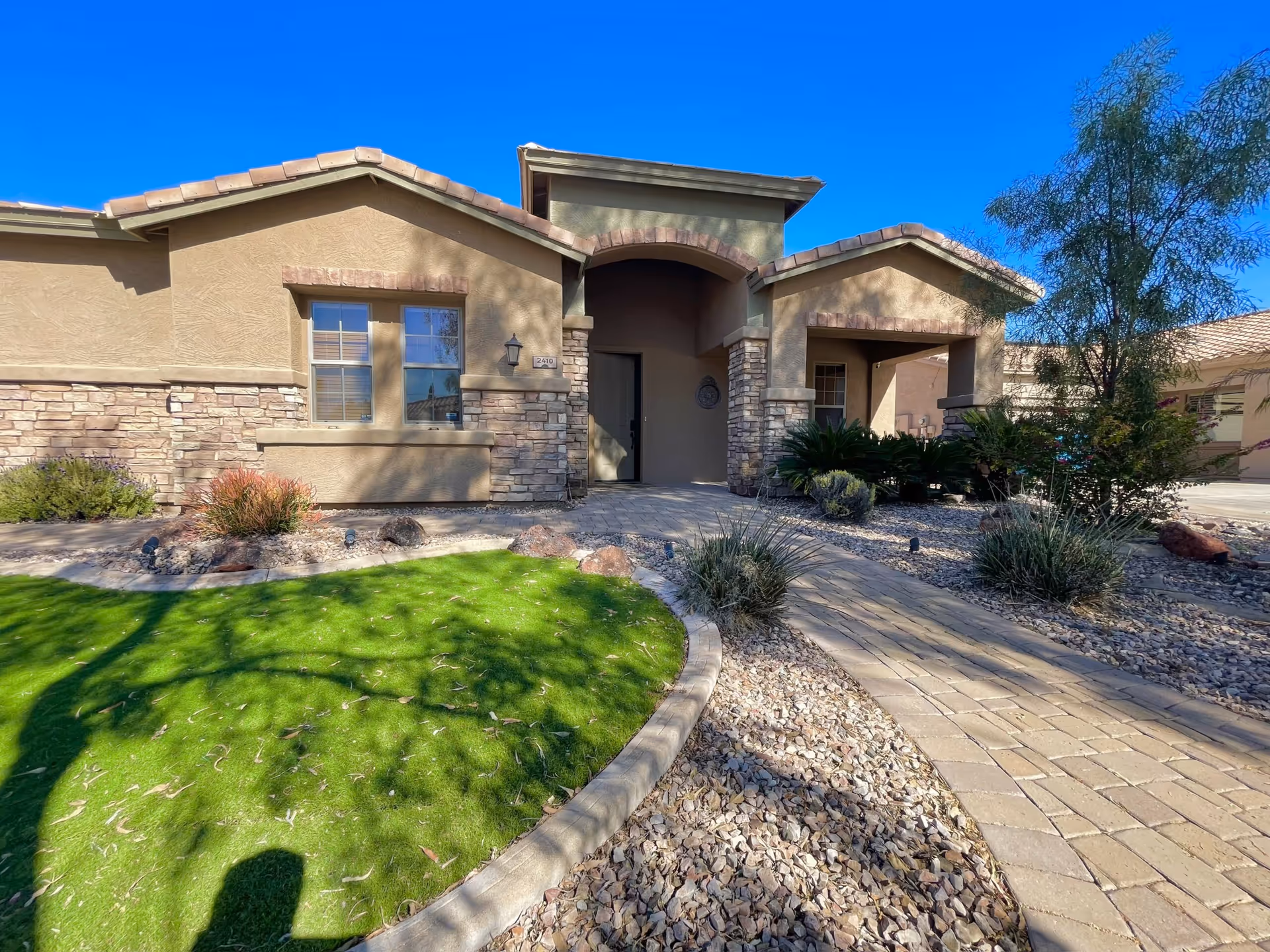 Front view of a beige assisted living facility with stone accents and a curved walkway leading to a covered entrance.