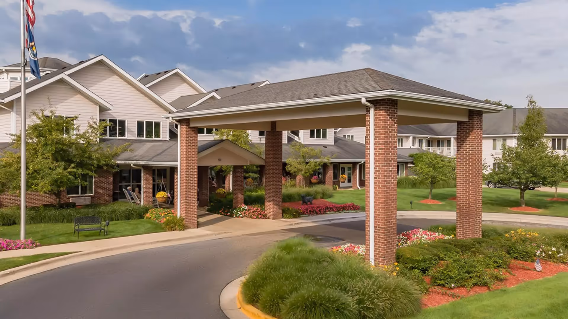 Brick entrance with a covered drop-off, brick pillars, and manicured landscaping at StoryPoint Grand Rapids West.