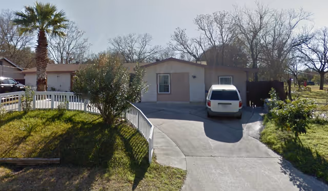 Front view of a single-story Mendoza #2 Assisted Living building with driveway and parked car.