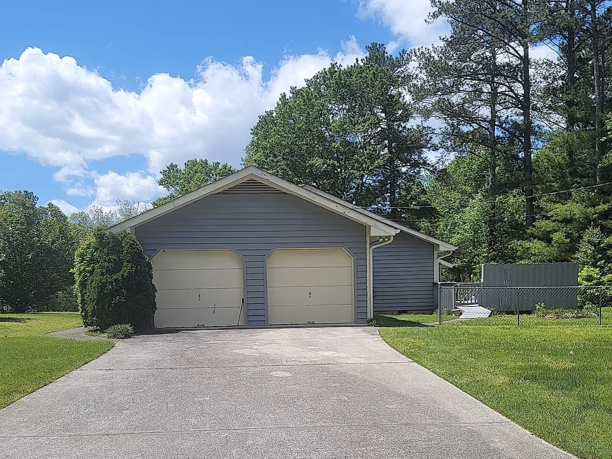 Blue, single-story home with two-car garage, driveway, and surrounding trees.