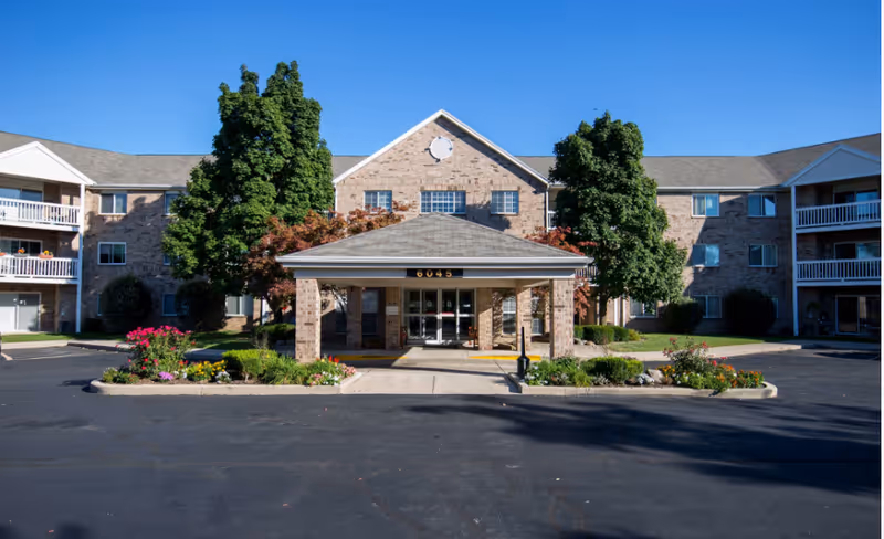 Exterior view of Siena Village facility with brick building, entrance, landscaping, and parking lot.