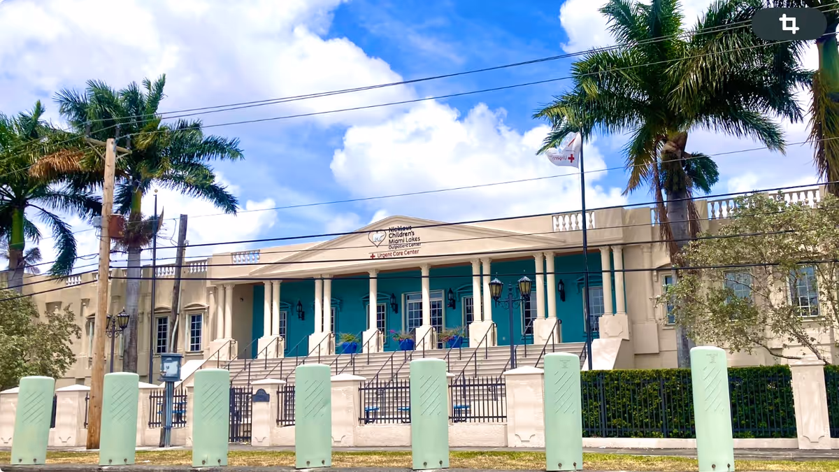 Front view of a beige medical facility with turquoise doors and palm trees.