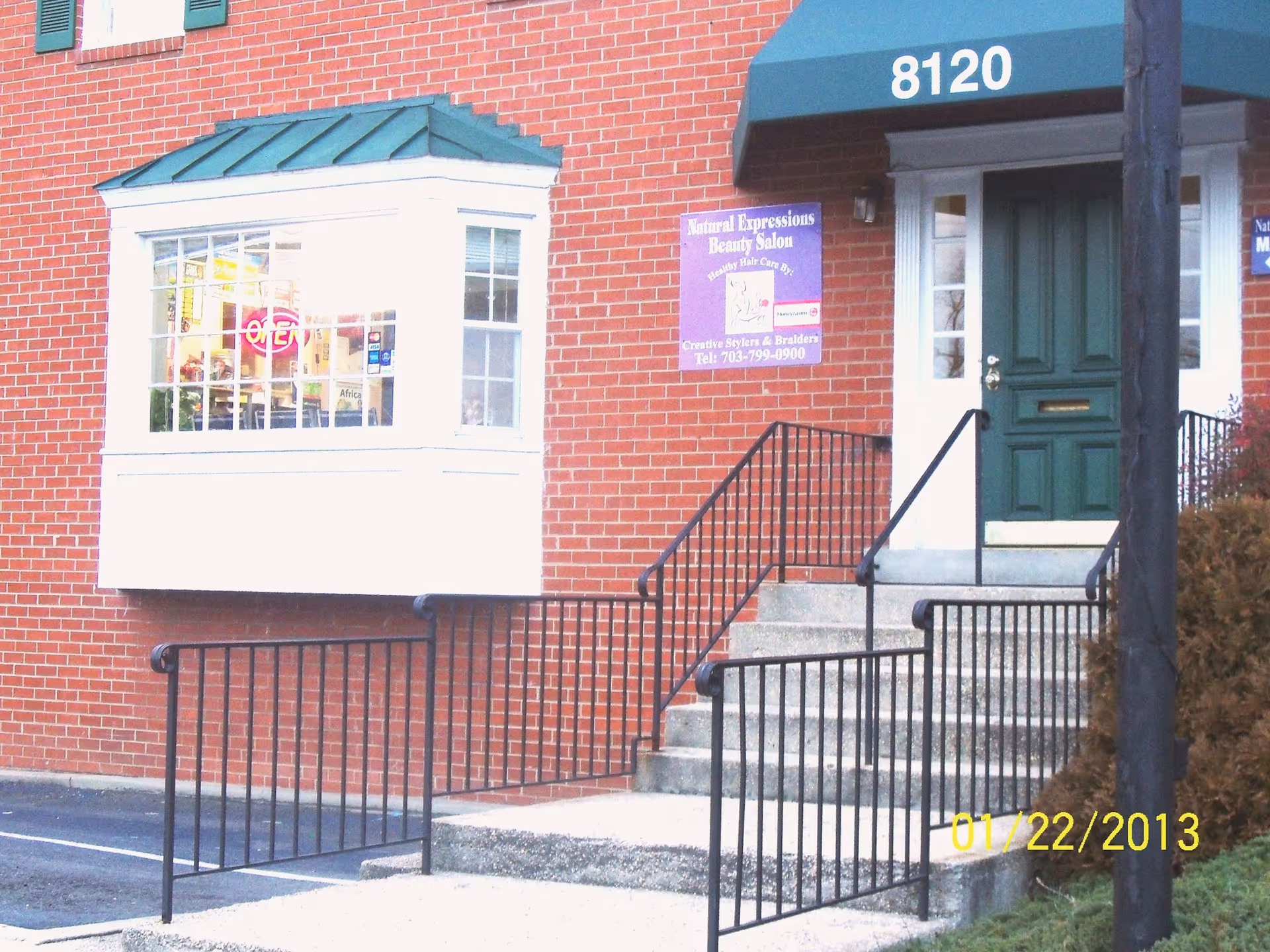 Brick exterior with green door, stairs, rails, and salon storefront window.