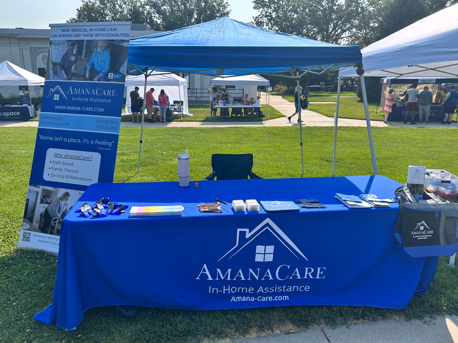 Outdoor booth for AmanaCare with a blue table and banner on grass.