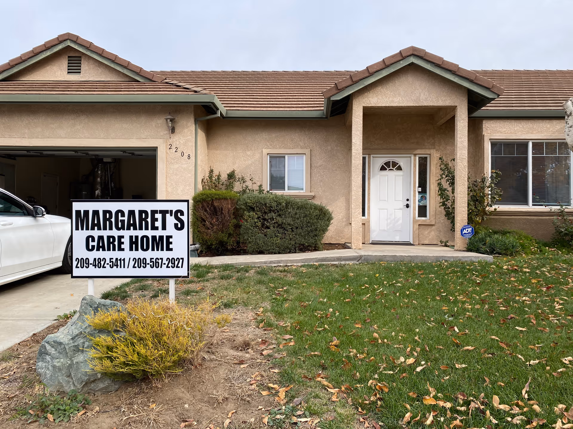 A beige single-story home with a white front door and a large Margaret's Care Home sign.