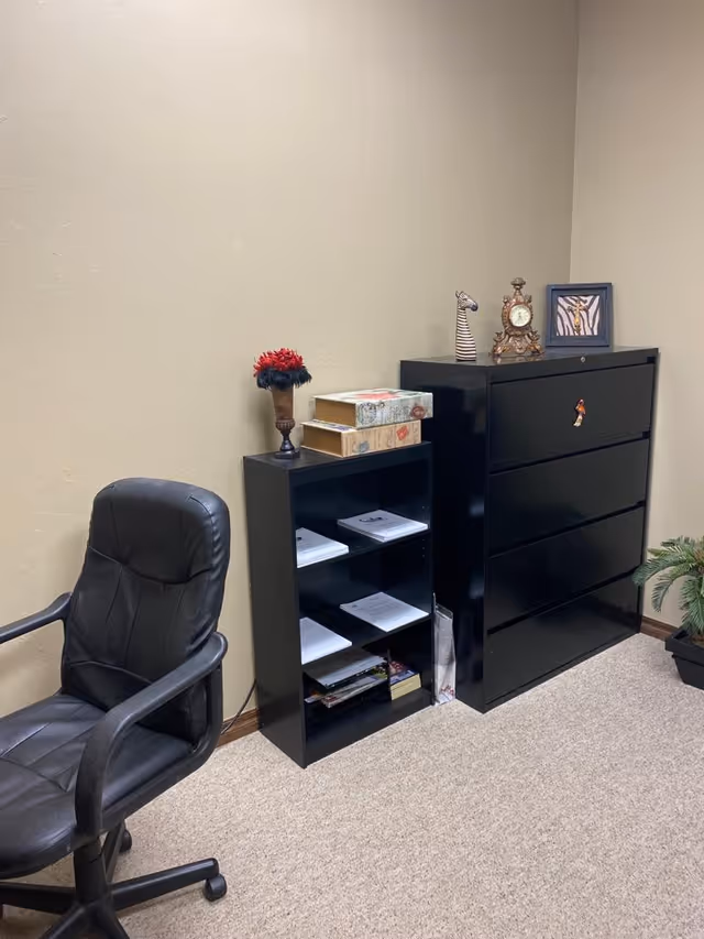 Office corner featuring a black chair, tall dresser, and small cubby shelf with papers.