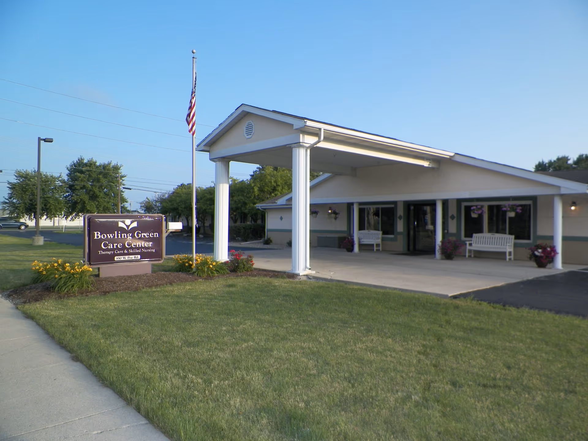 Exterior view of Bowling Green Care Center entrance with benches, sign, and American flag.