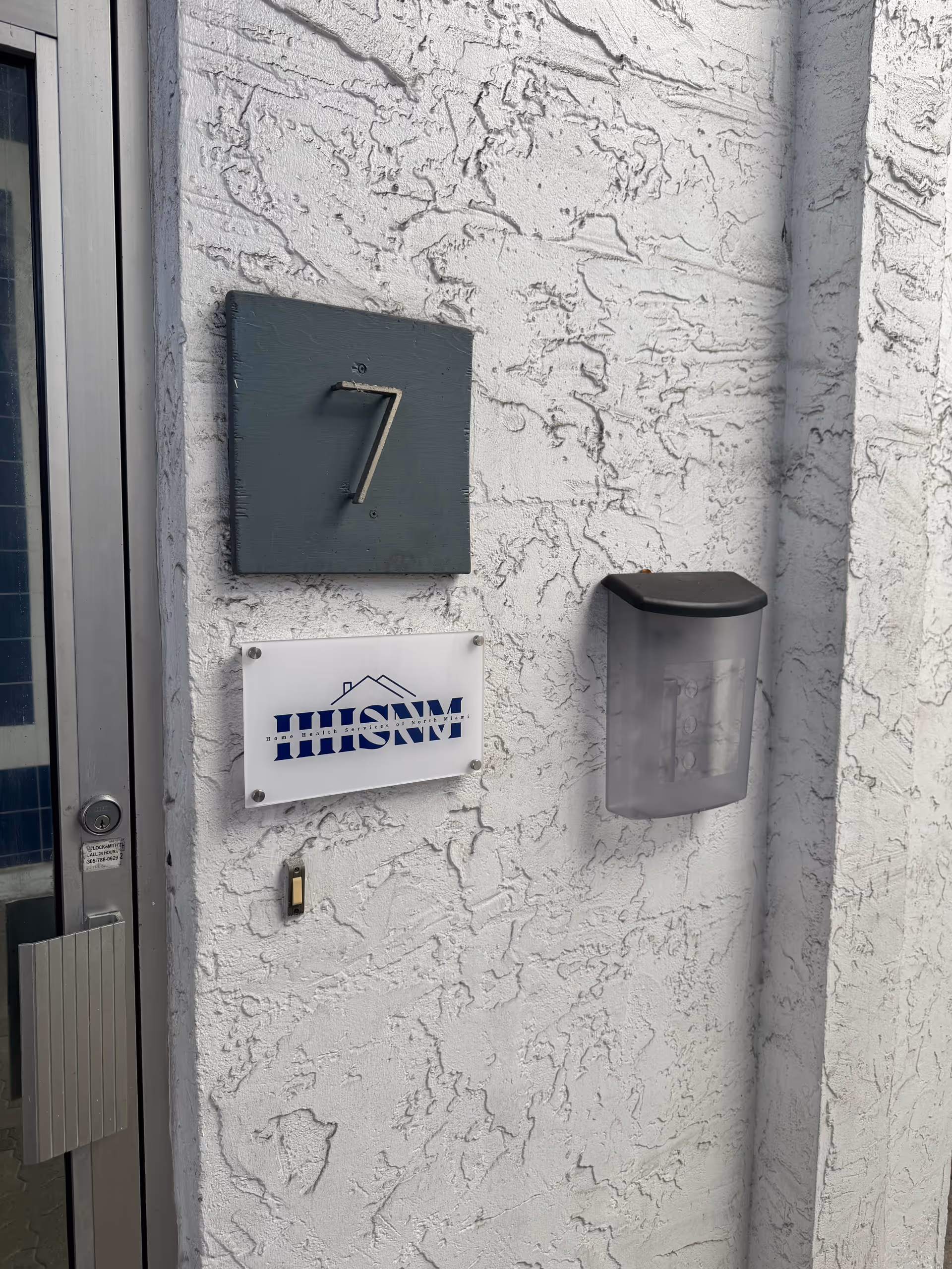 Exterior entrance of a senior living facility with door, number 7 plaque, and HHSNM sign.