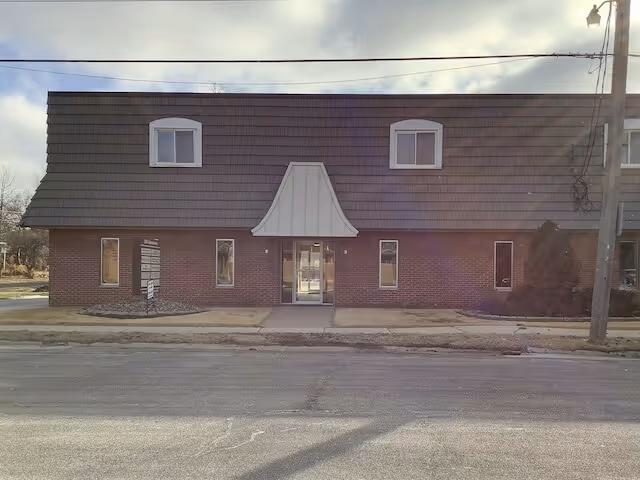 Exterior view of a brick building with a sloped roof and two dormer windows.