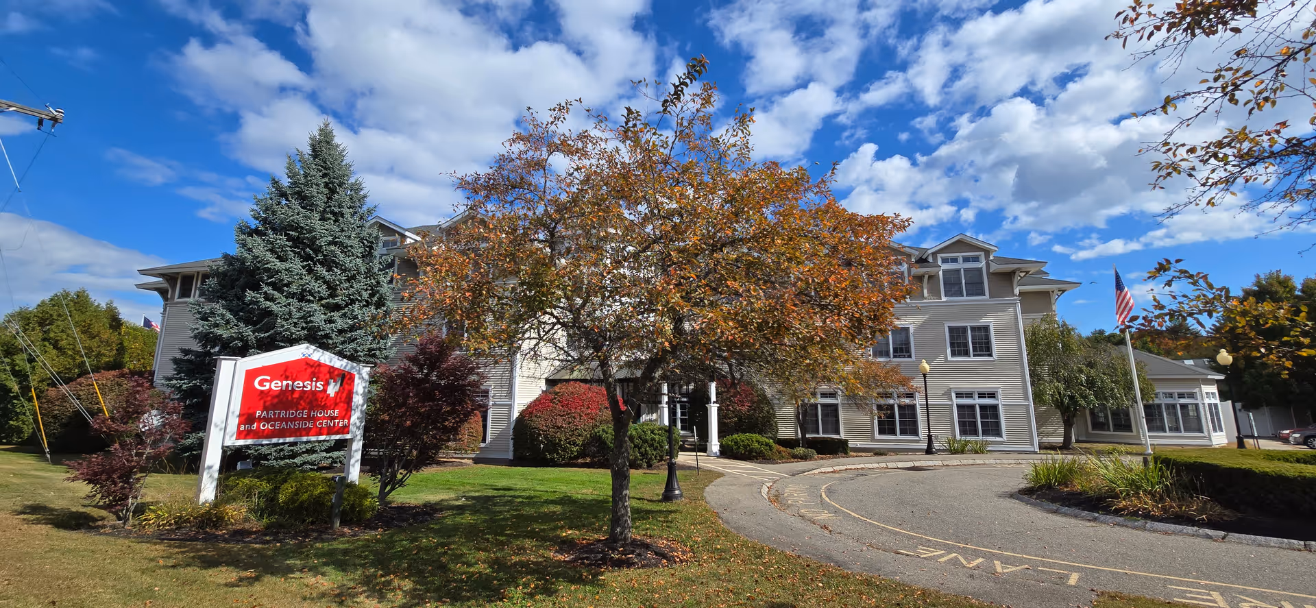 Exterior view of a multi-story senior living facility with a curved driveway and sign.