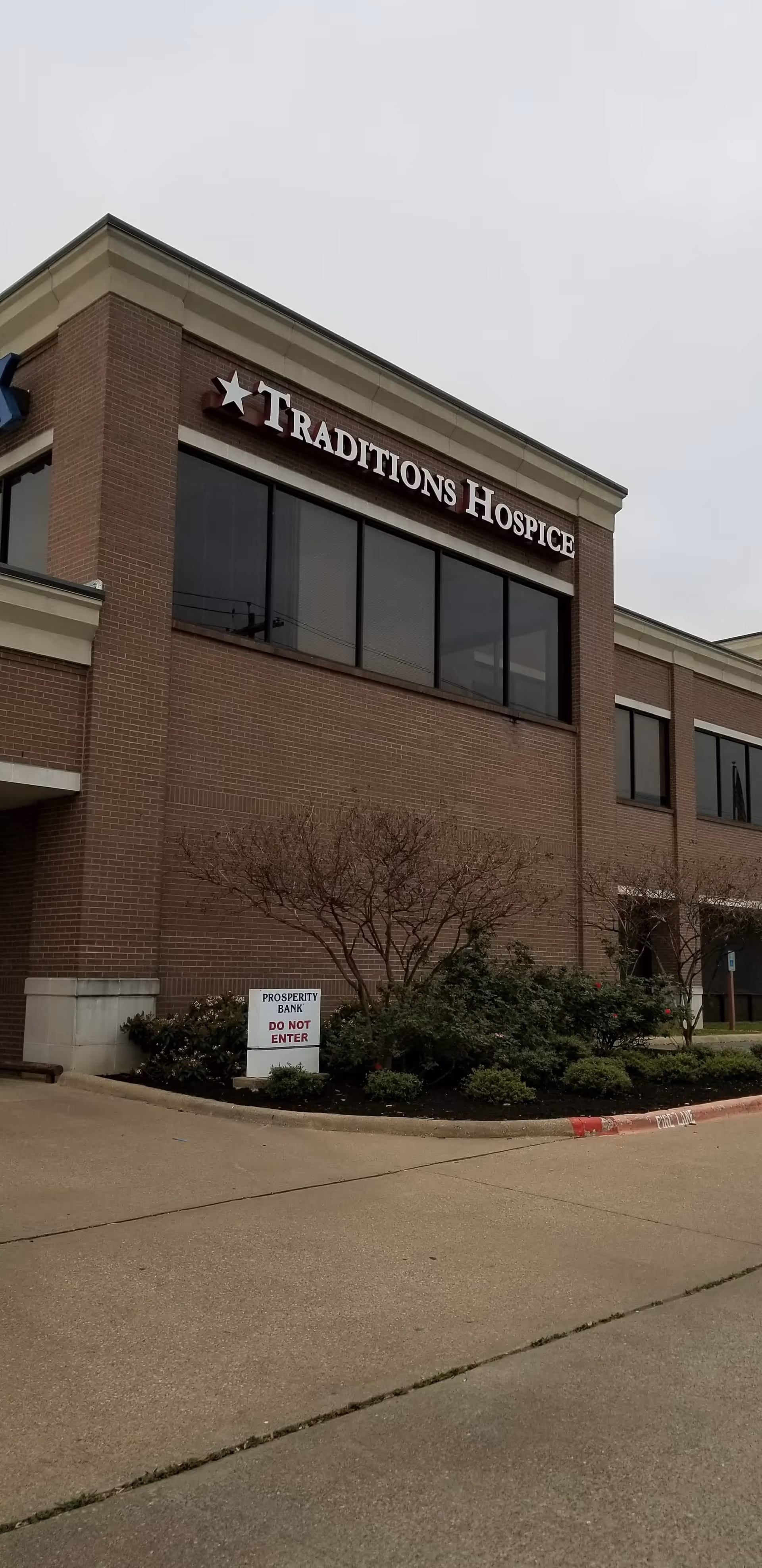 Brick building exterior with large windows and Traditions Hospice sign on the front.