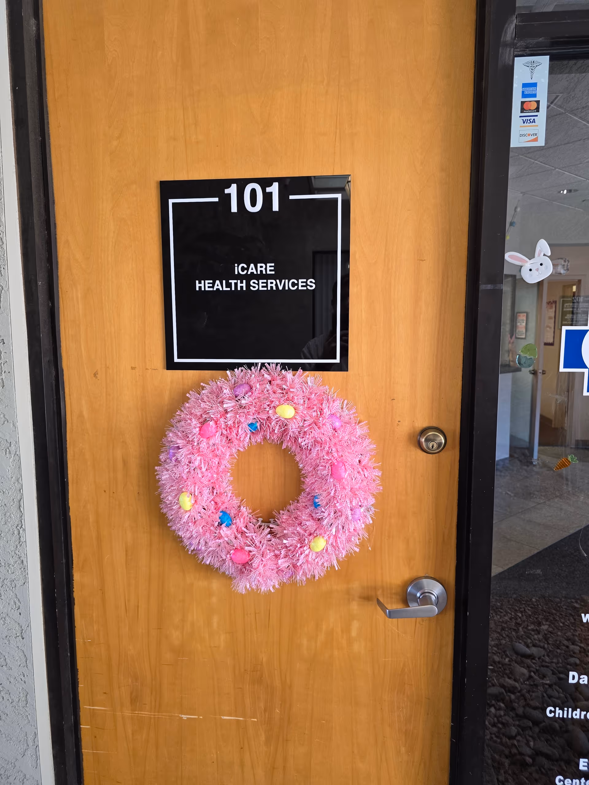 Wooden door with 101 sign and iCare Health Services tag, pink wreath attached