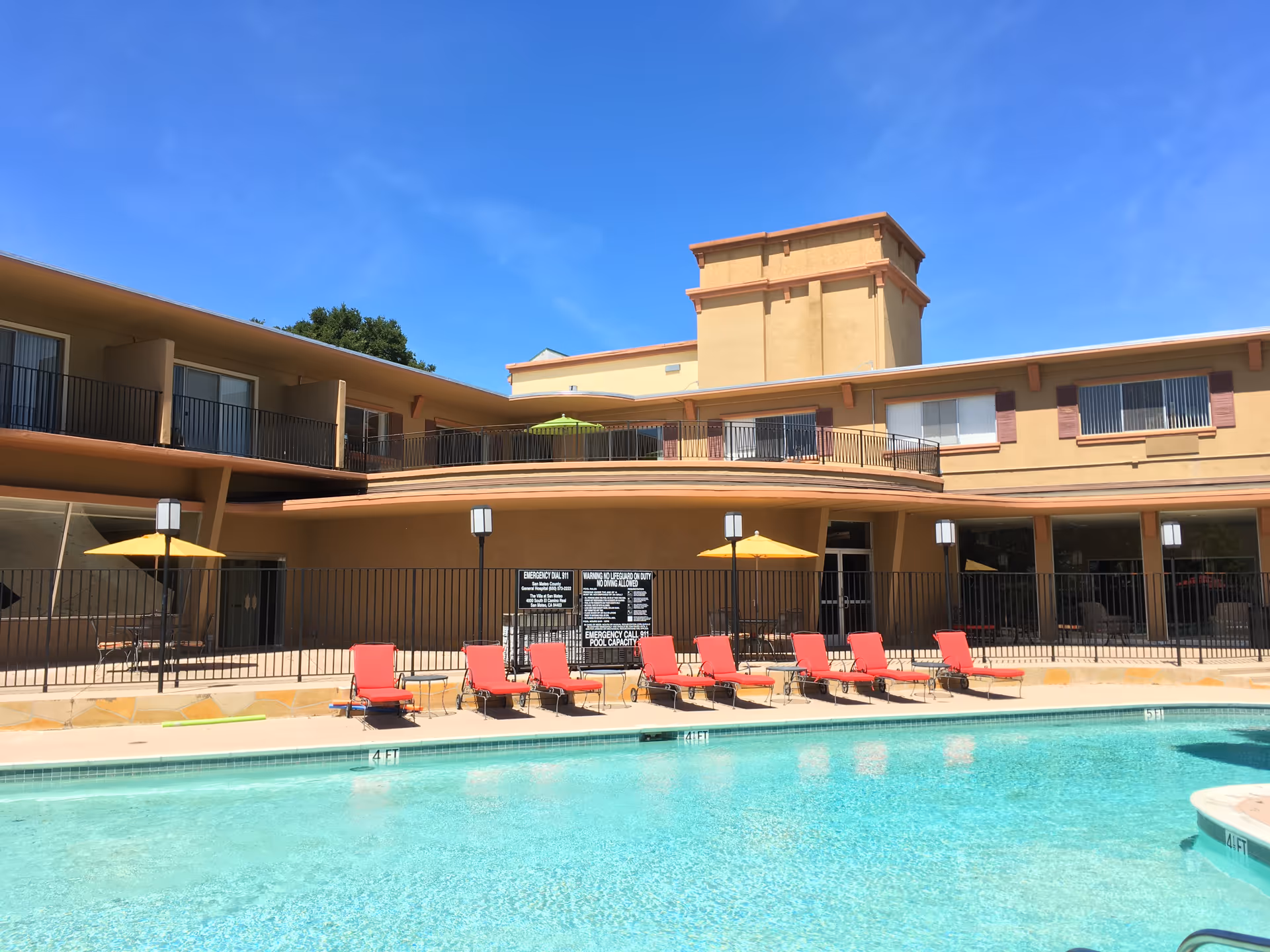 Exterior view of Villa at San Mateo with a pool, lounge chairs, and umbrellas.