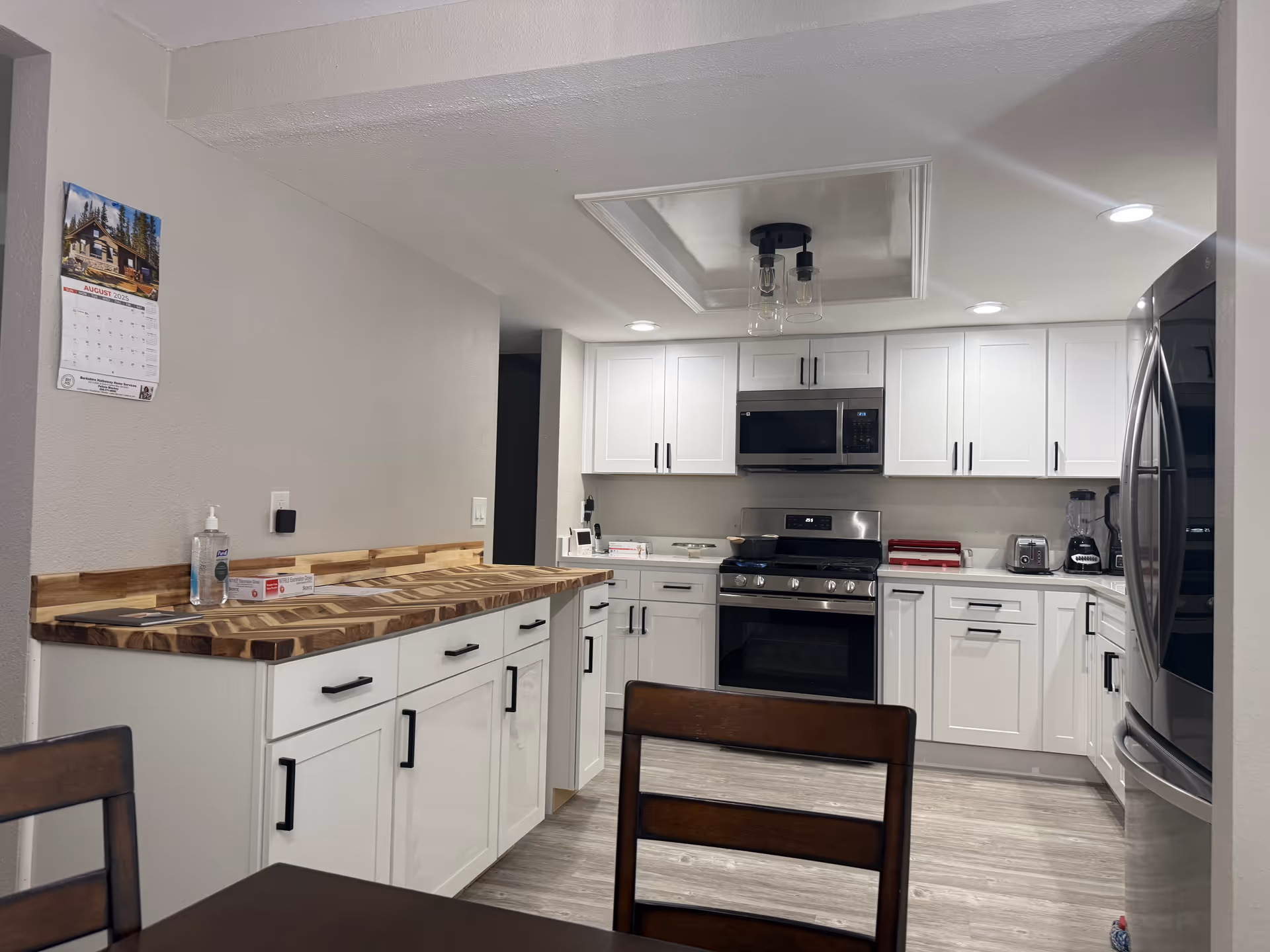 White kitchen with stainless appliances, wooden countertops, and dining chairs in a senior living home.