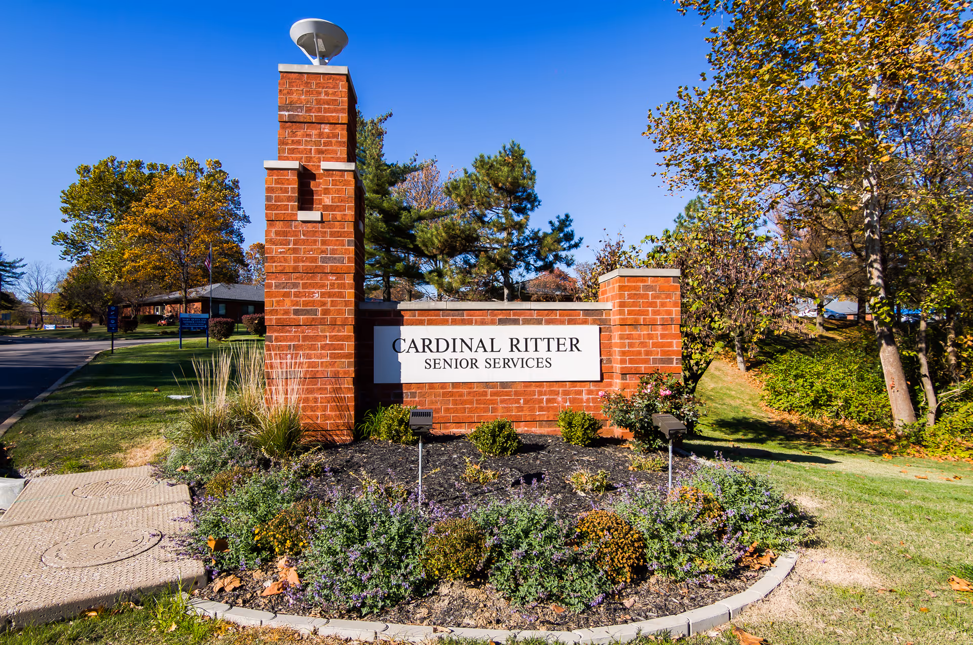 Brick sign for Cardinal Ritter Senior Services with landscaped beds and trees under blue sky.