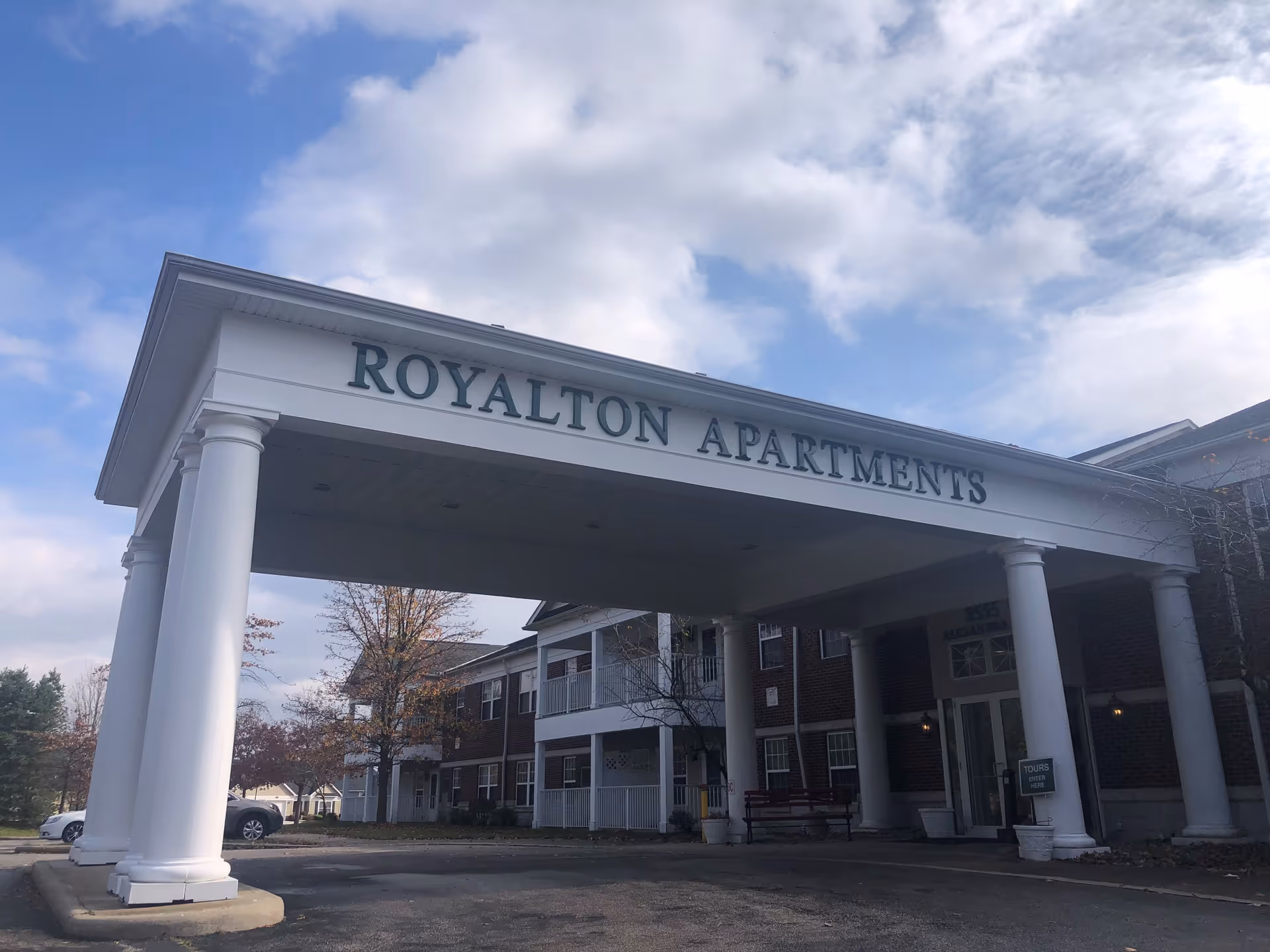 Covered entrance with white columns and a sign reading 'ROYALTON APARTMENTS' on a two-story brick residential building.
