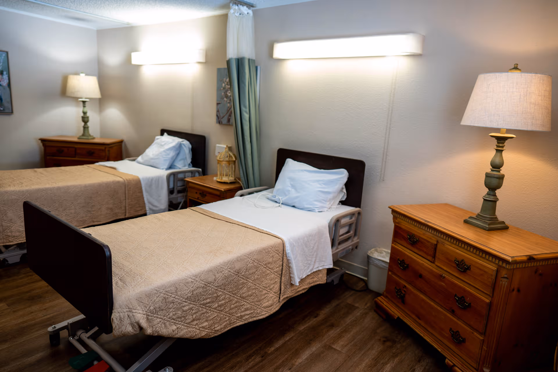 Two twin beds with beige bedspreads, nightstands, and lamps in a furnished senior living bedroom.