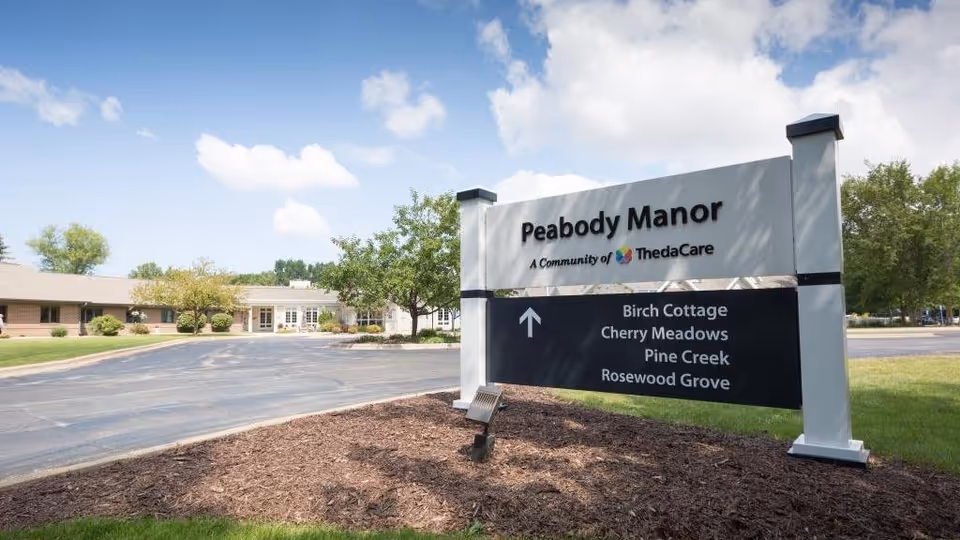 Large Peabody Manor sign with directional listings beside a parking lot and building.