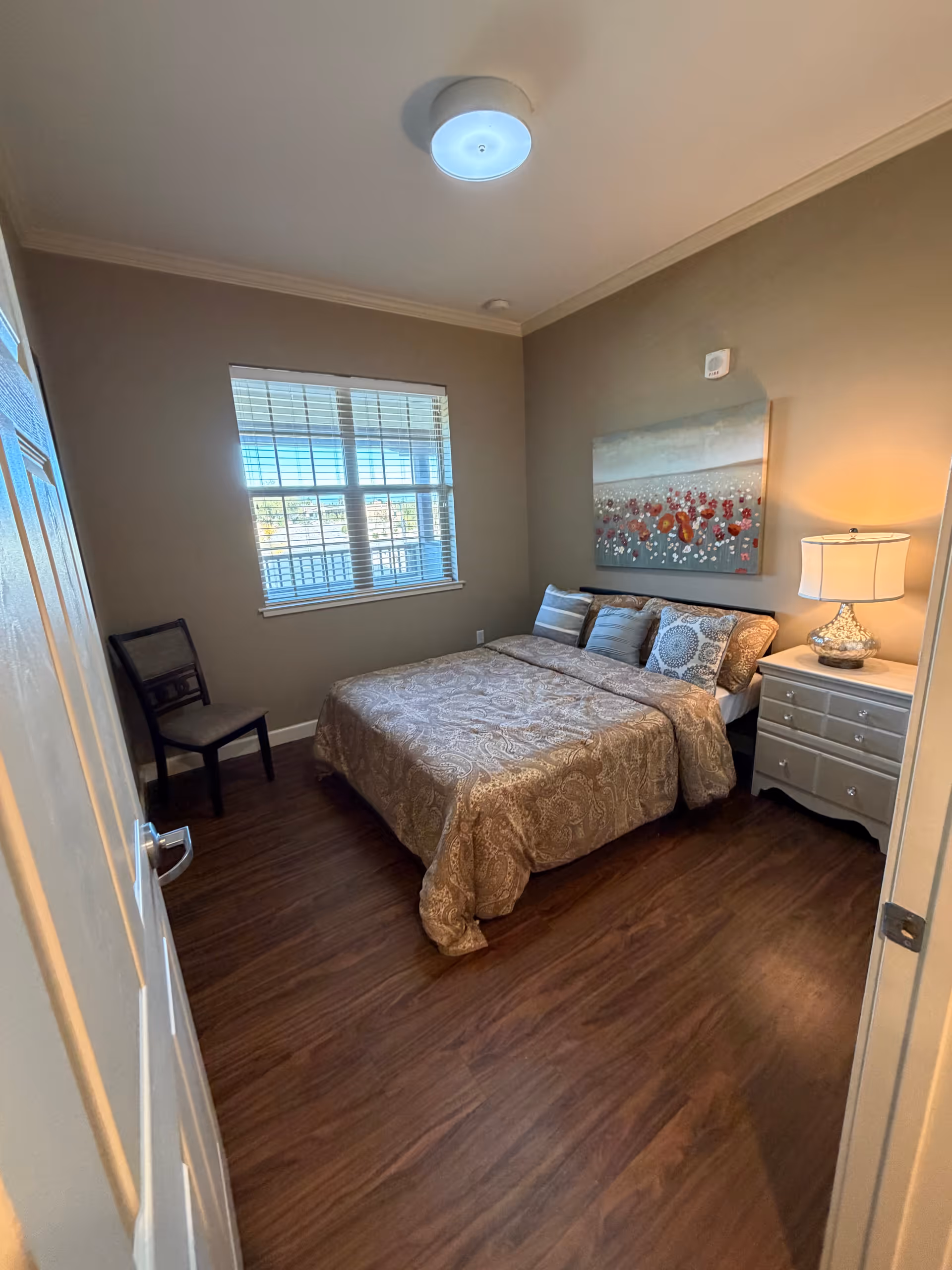 A tidy bedroom with a bed, nightstand, lamp, wall art, and window.