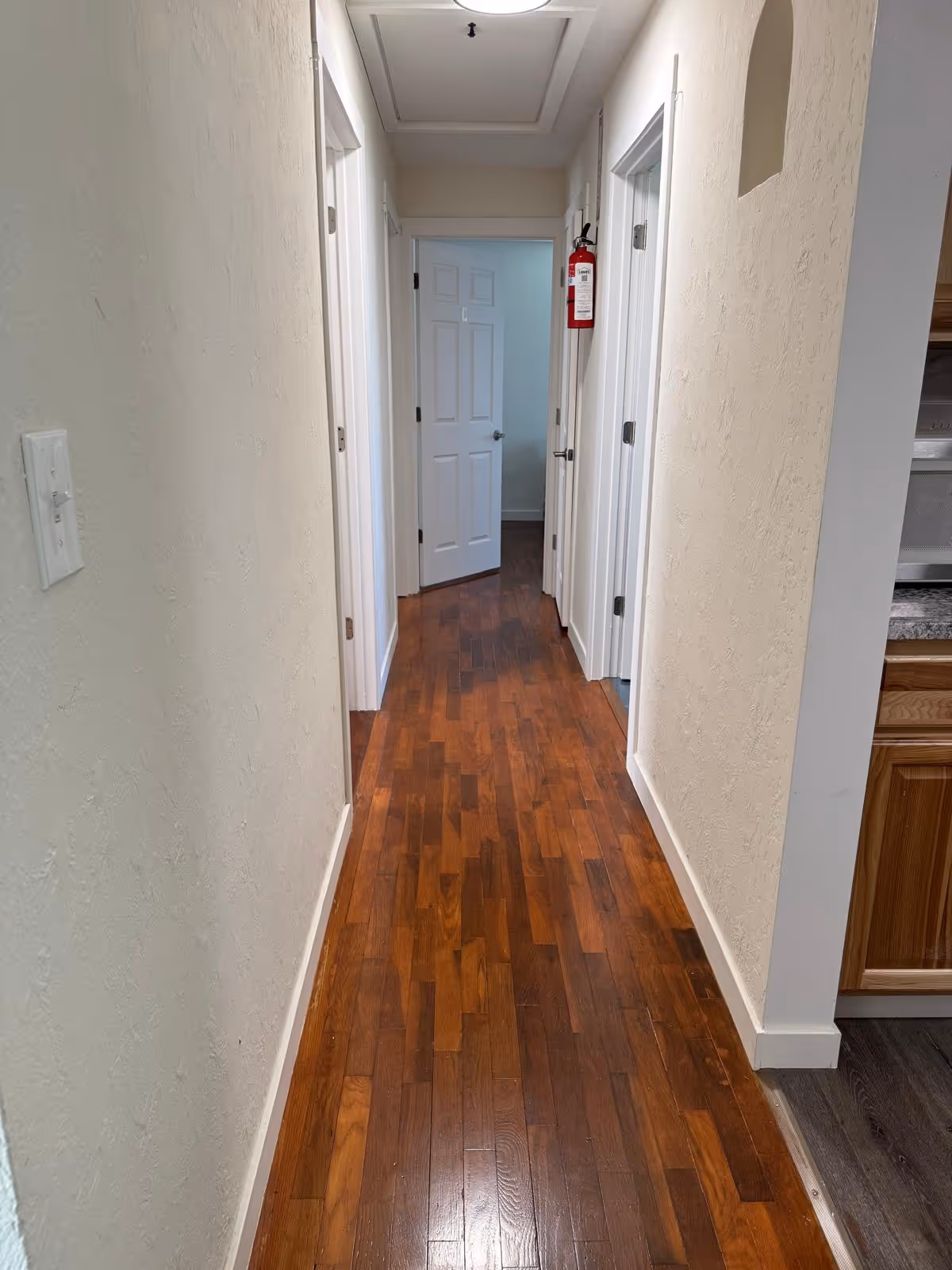 Narrow indoor hallway in a senior facility with closed doors, wood flooring, and a fire extinguisher.