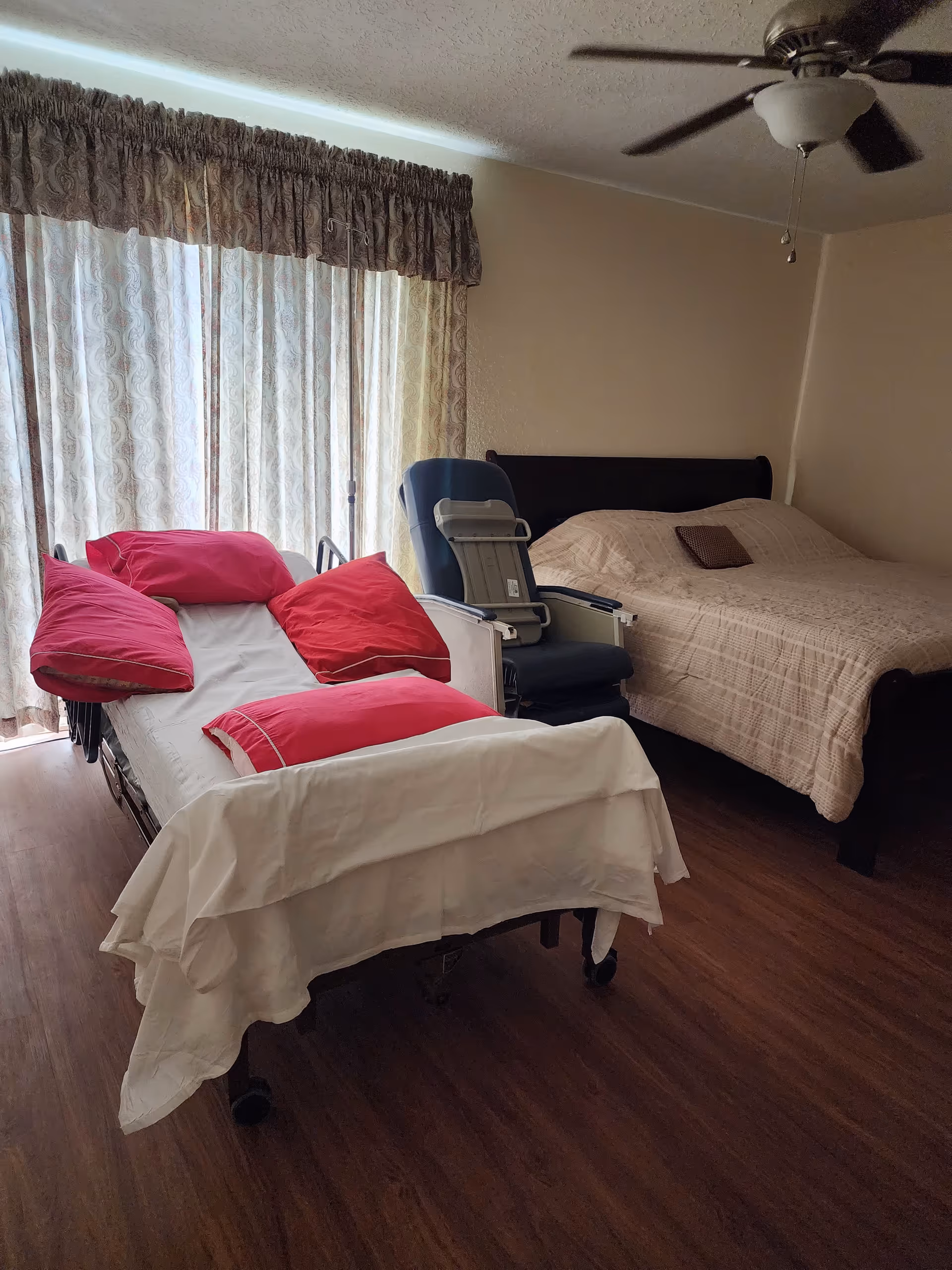 A senior facility patient room featuring two beds, curtains, and a ceiling fan.