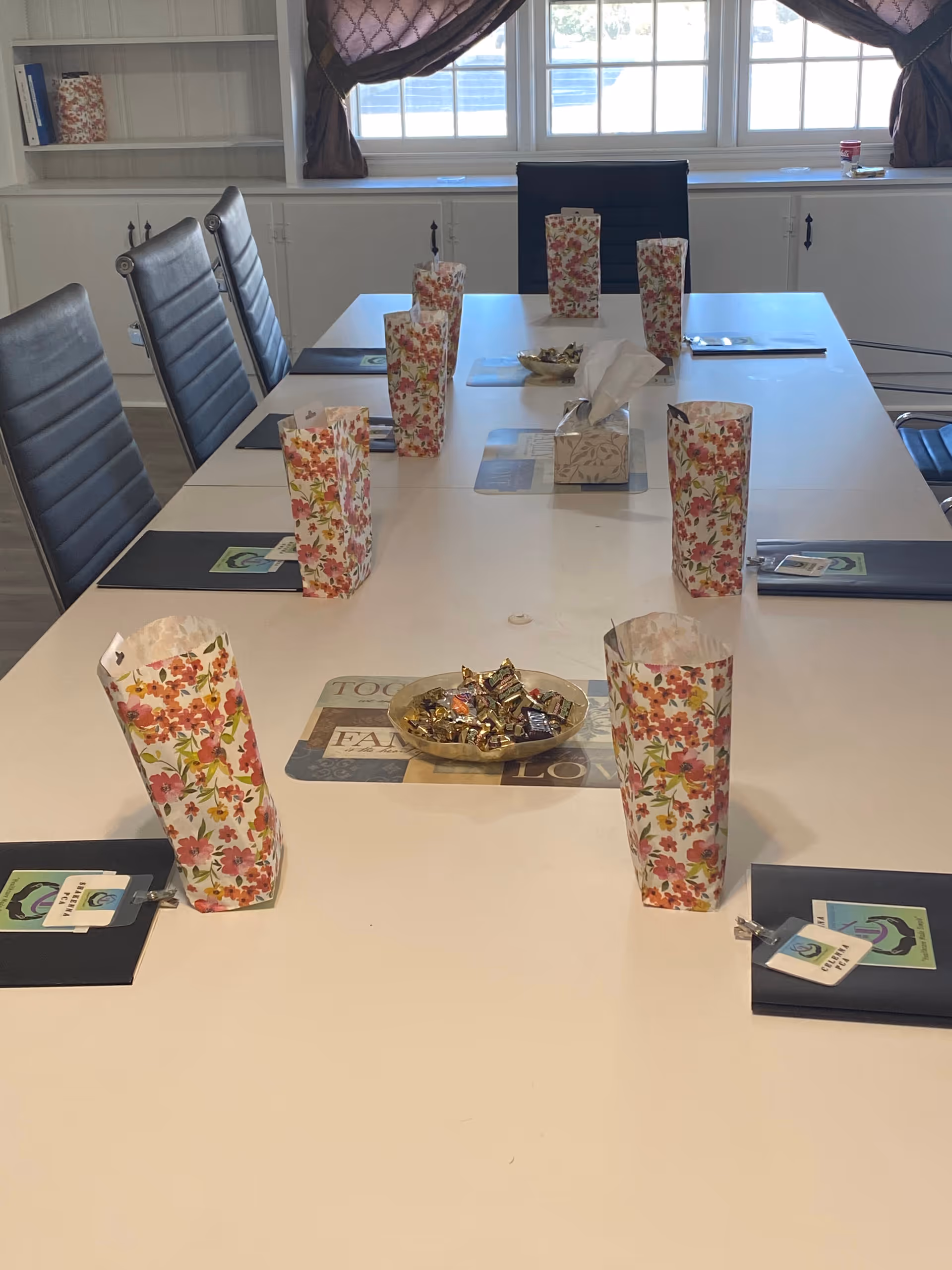 A long dining table set with floral napkin holders and place mats.