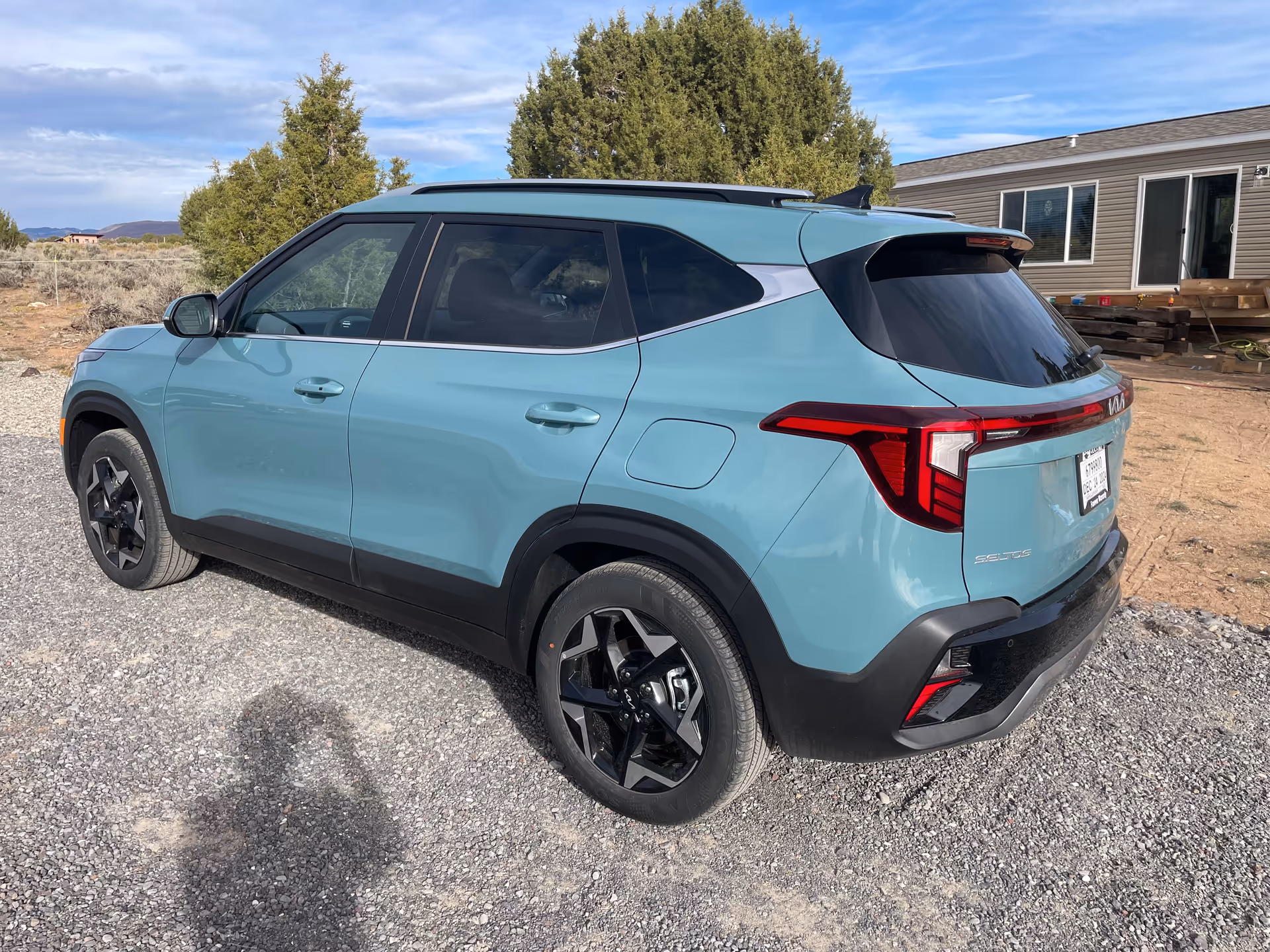 Turquoise SUV parked on a gravel lot with a beige modular home in the background