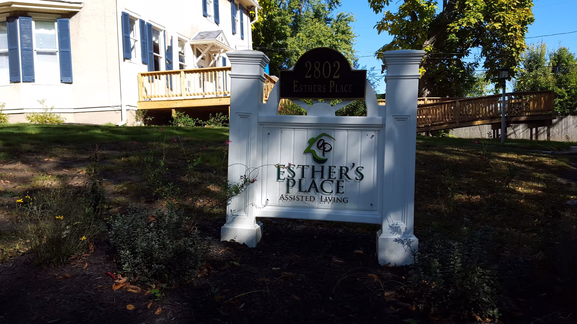 White sign for Esther's Place Assisted Living in front of a house exterior.