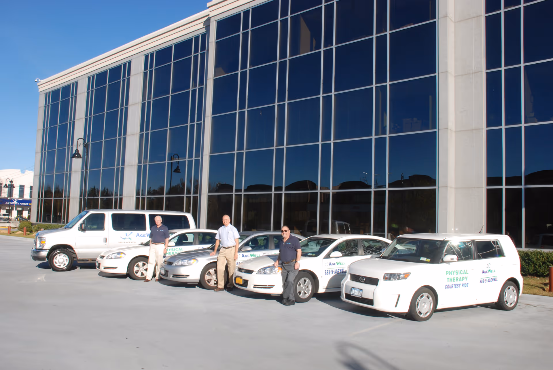 Exterior view of AgeWell Physical Therapy and Wellness facility with branded vehicles and staff