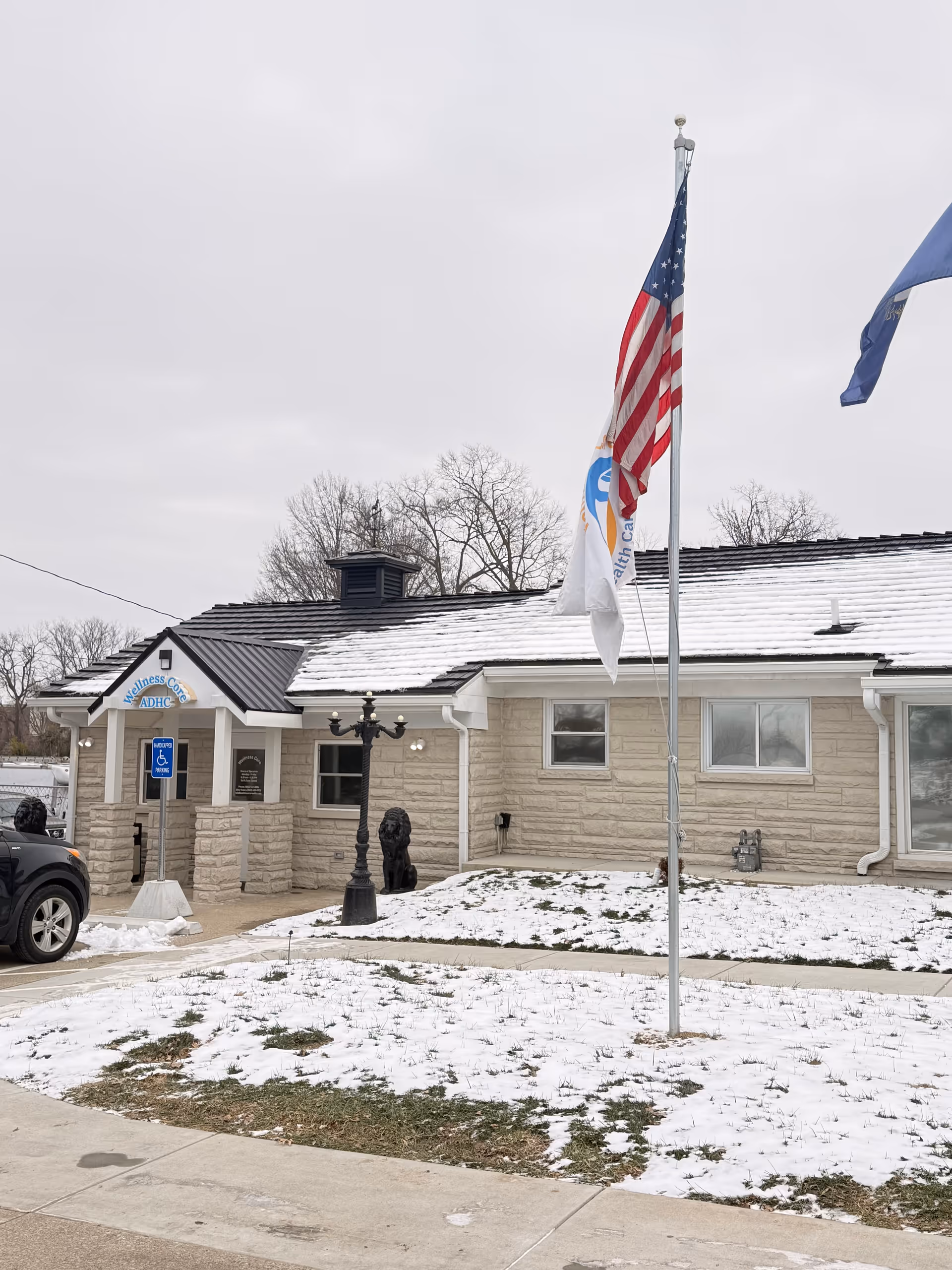 Exterior view of Wellnesscore ADHC facility with flags, snow, and entrance.