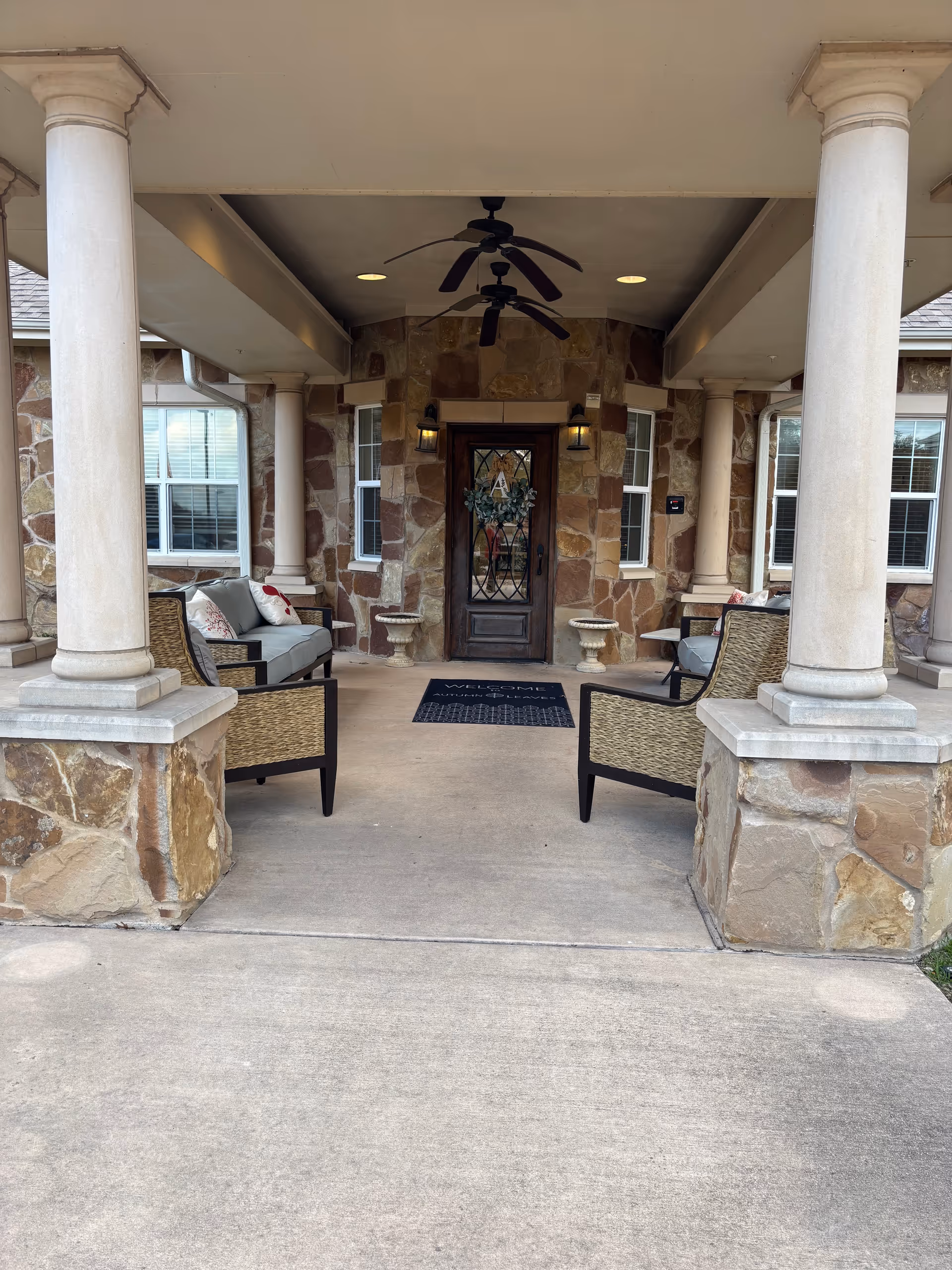 Stone front entrance with columns, outdoor seating, and wreath on door.