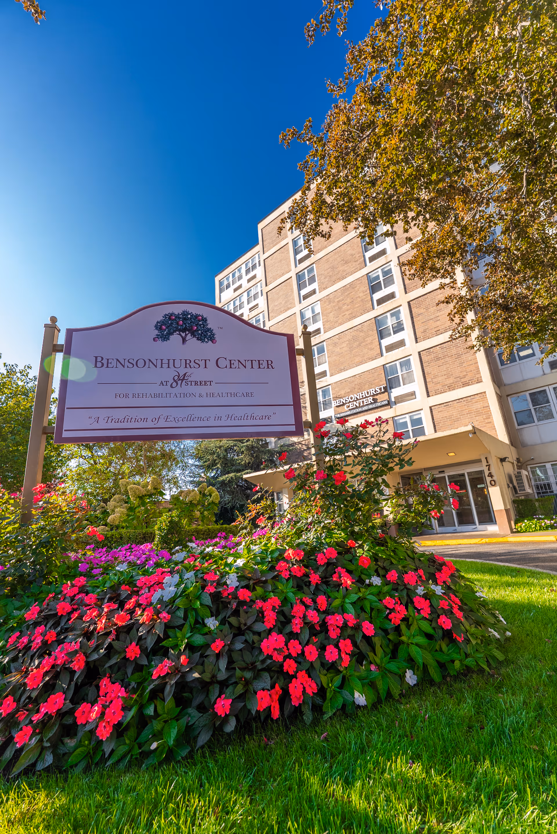Exterior view of Bensonhurst Center for Rehab and Healthcare with blooming flowers and sign.