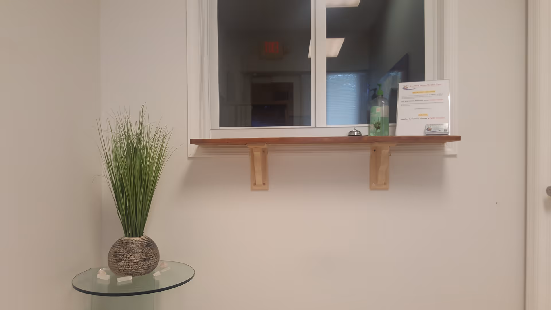 Interior reception area with a windowed counter, wooden ledge, and tall potted plant.