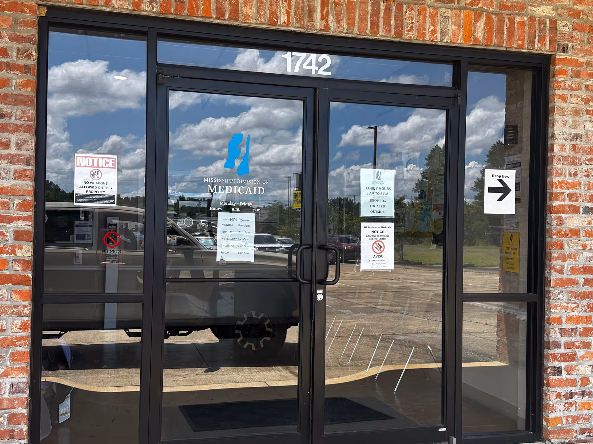 Brick storefront with glass doors labeled Mississippi Division of Medicaid and posted notices.