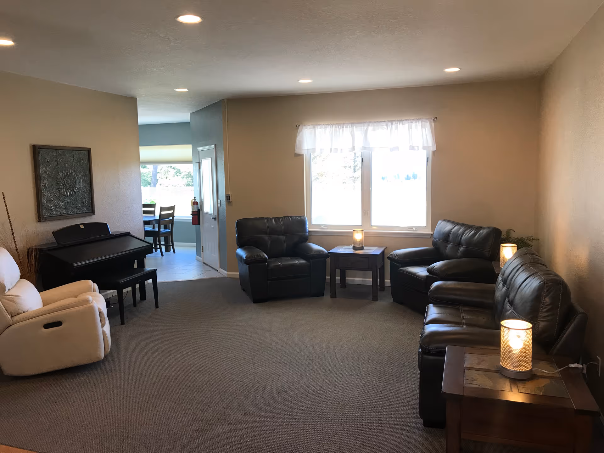Bright senior living common area with black leather seating, piano, and windows.