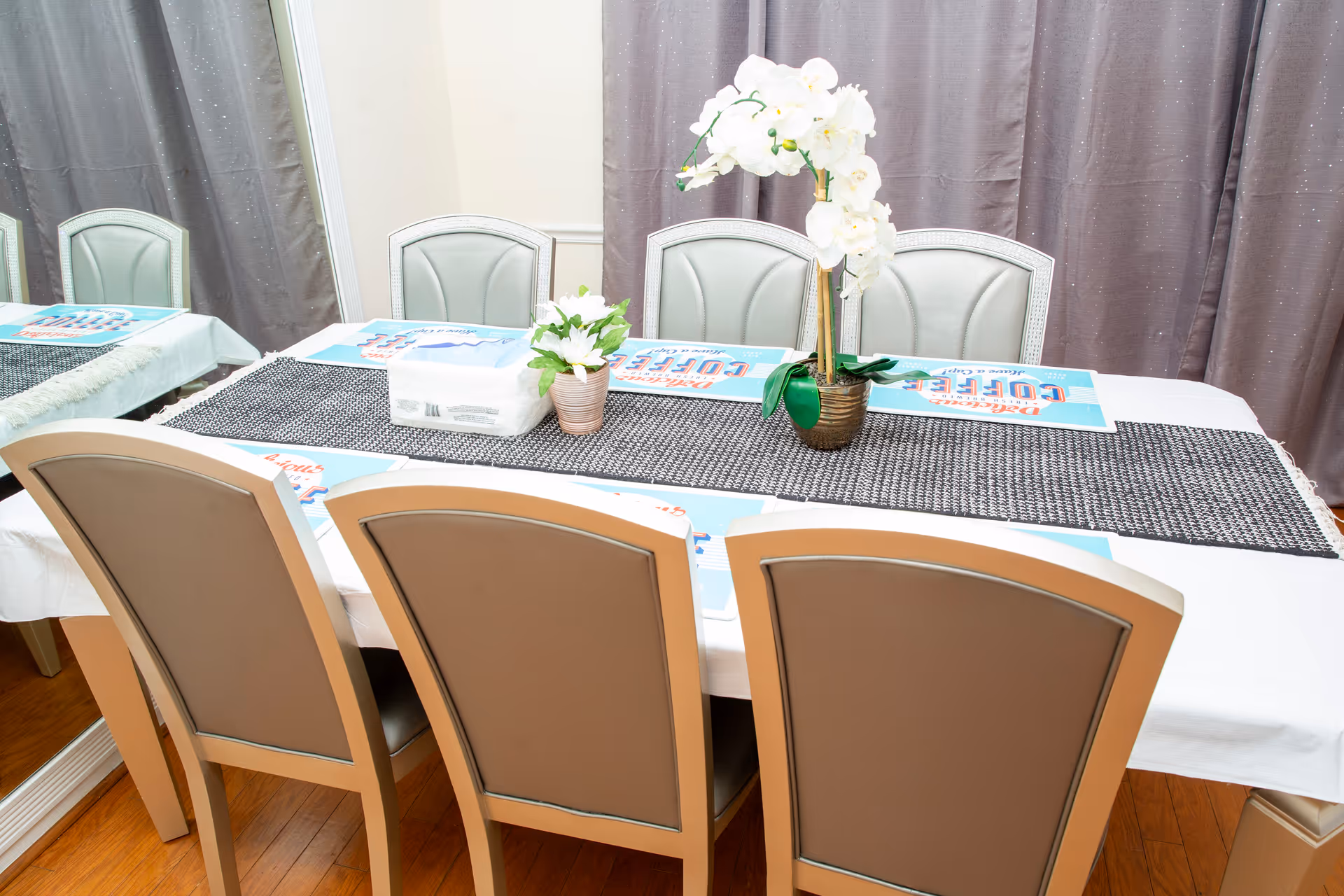 A long dining table with chairs and a flower centerpiece in a bright dining room.