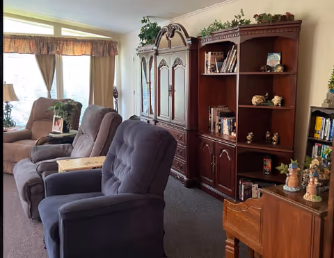 Cozy senior living room with recliners, a large wooden cabinet, and bookshelves.