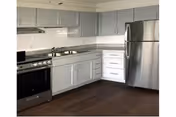 Modern L-shaped kitchen with light gray cabinets, stainless steel appliances, and dark wood flooring.