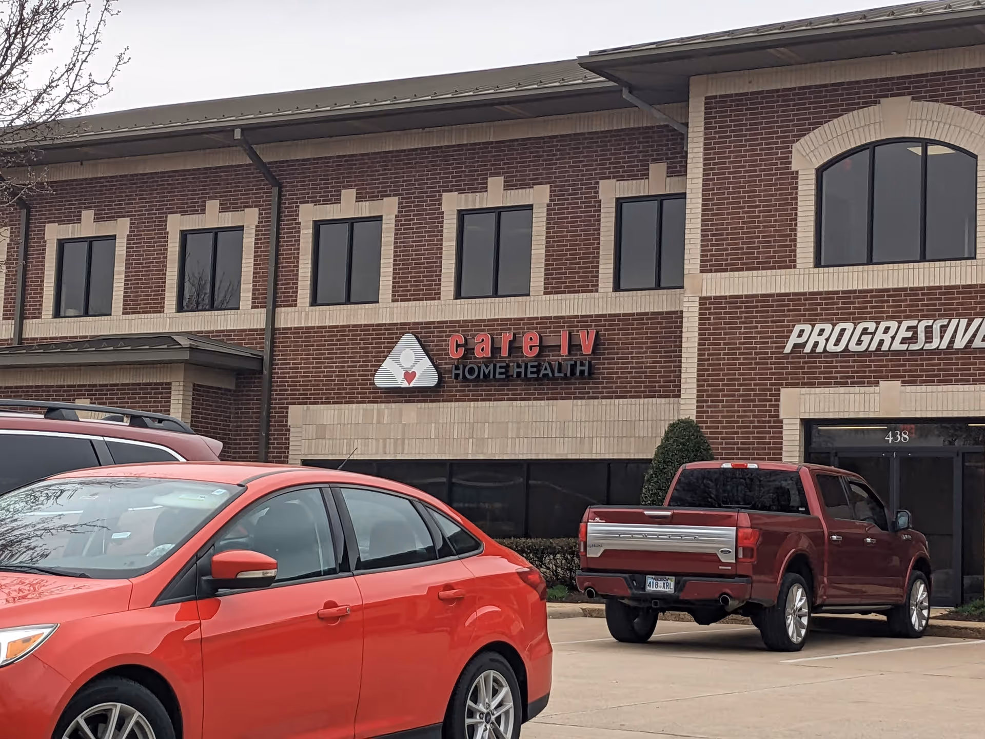 Brick storefront building with Care IV Home Health sign and parked red cars.